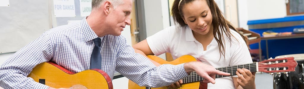 Schoolgirl and teacher playing acoustic guitar in music class